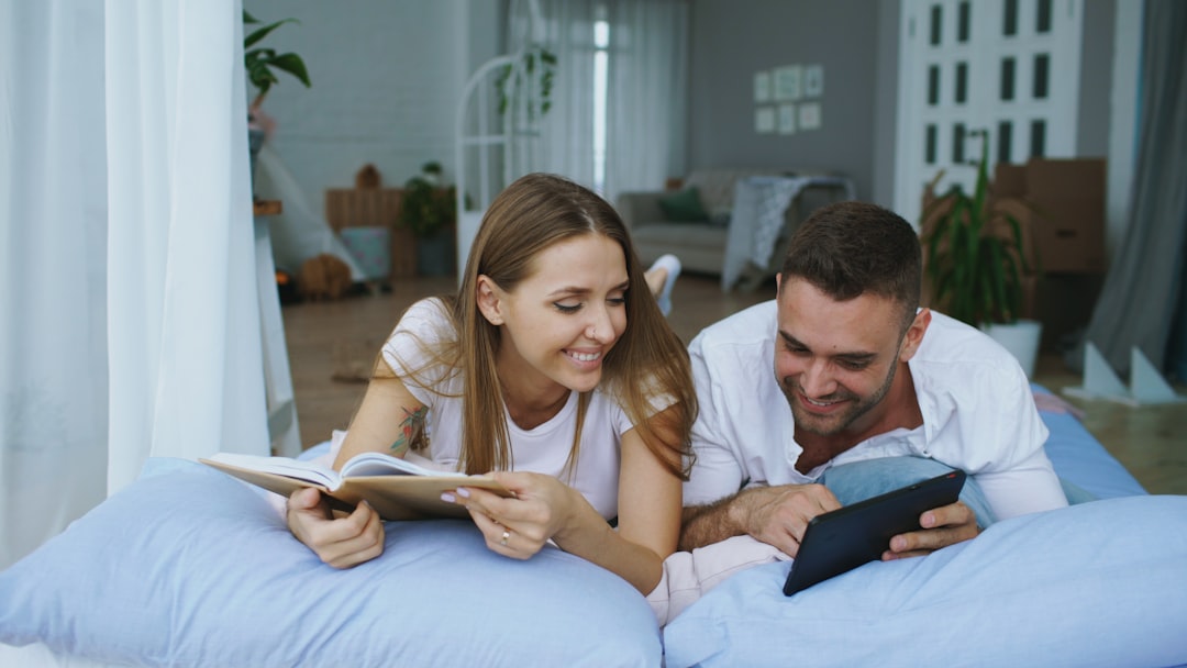 A happy couple sits together in a bright, modern living room, excitedly reviewing the architectural plans for their new dream home.