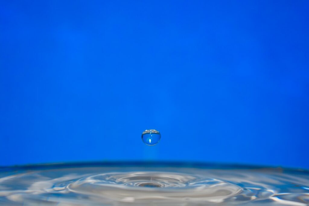 Minimalist close-up of a water droplet hitting a calm surface, creating expanding concentric ripples that symbolize the co...