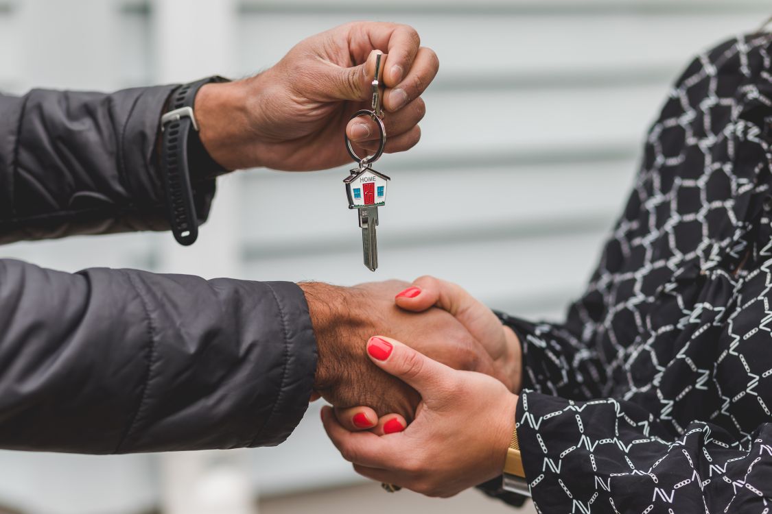 A professional real estate agent hands keys to a smiling, happy couple standing in the entryway of a bright, modern new home.