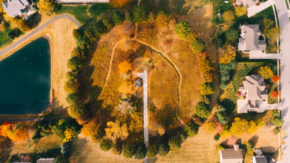 A clean, paved road splits into two separate paths through a beautiful, manicured residential neighborhood, representing a crucial financial decision for homeowners.