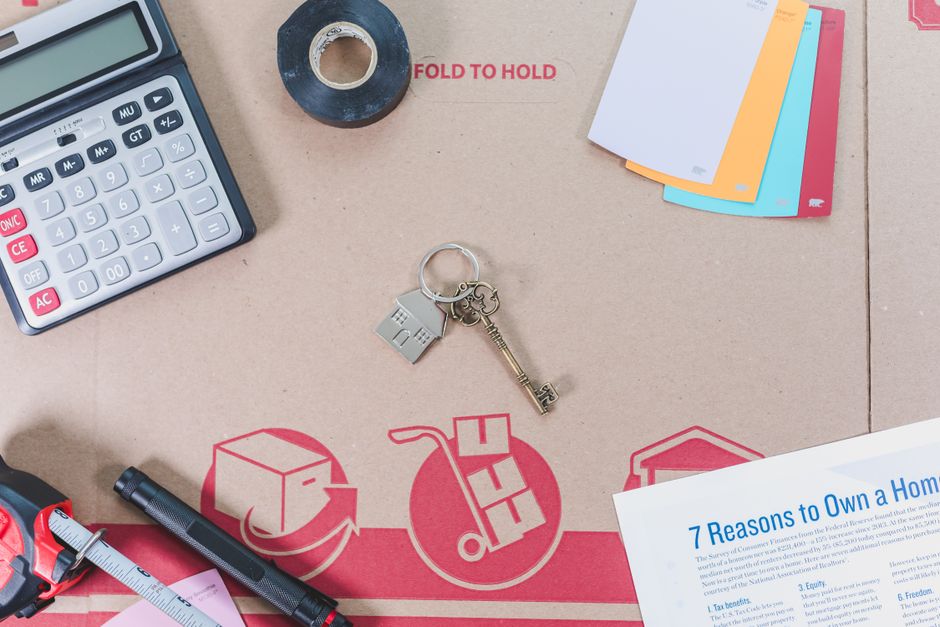 Professional and clean flat lay of a calculator, a set of house keys, and a pen on a modern wooden desk, representing the ...