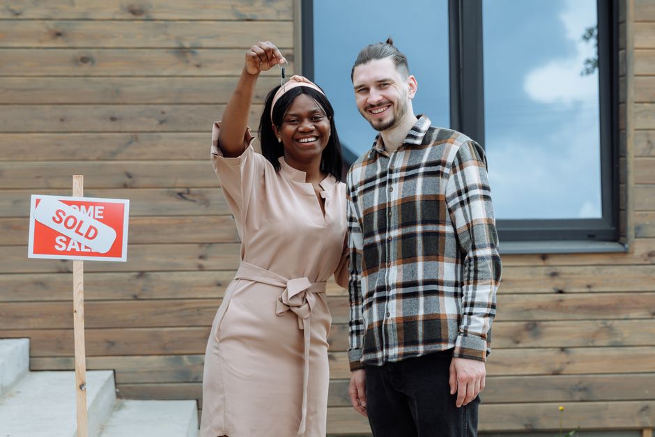 A smiling person stands in front of their new home, proudly holding up a set of house keys to symbolize a successful and profitable sale.