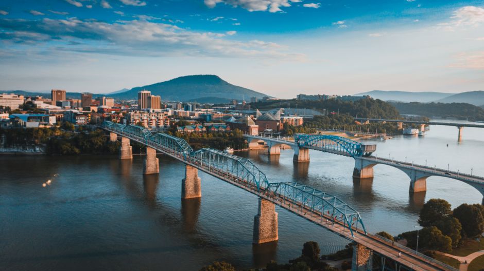 A stunning, high-angle photograph of the Chattanooga, Tennessee skyline and the Tennessee River, captured on a bright, sunny day from a scenic mountain overlook.